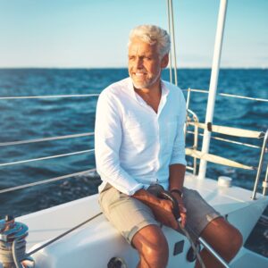 Mature man sitting on the deck of his boat enjoying a sunny day sailing on the open ocean